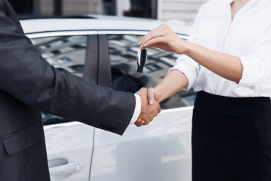 Buying new car. Handshake and handing over keys by consultant to buyer
