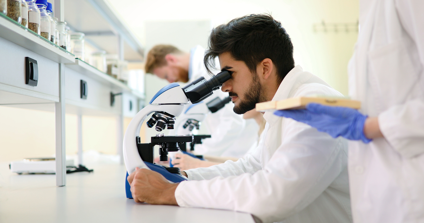 Young male scientist looking through microscope in laboratory
